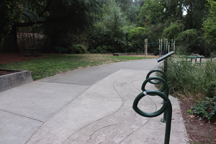 Bike racks &ndash; two picnic benches, on pavement & under tree on natural surface &ndash; playground with bark-chip surface